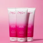 Három rózsaszín-fehér Curly Secret Volume+ Styling Gel hajformázó zselé vízcseppes flakonja rózsaszín háttér előtt.