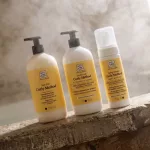Soivre Curly Method sárga címkés göndör hajápoló termékek: Low-Poo sampon, balzsam és formázó hab egy kőperemen.