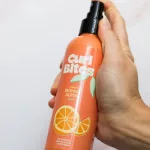 Kézben tartott narancssárga Curl Bites frissítő spray fekete adagolófejjel és narancs mintával.