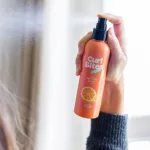 Egy kéz megnyomja a Curl Bites 2 Minute Refresh Spray flakonjának adagolófejét, ahogy finom permetet fúj a hajra.