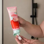 Rózsaszín tubusos Curl Bites Weightless Detangling Conditioner hajbalzsam piros alma illusztrációval és világoszöld kupakkal tenyérbe adagolása tubusból.