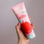Kézben tartott rózsaszín Curl Bites Weightless Detangling Conditioner hajbalzsam tubus piros alma mintával.