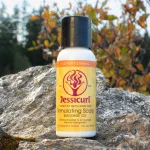 Jessicurl Stimulating Scalp Massage Oil tápláló fejbőrolaj fehér flakonban, egy sziklán elhelyezve.