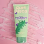 Curl Bites Rosemary mélytisztító sampon zöld tubusban, rozmaring illusztrációval, rózsaszín habos háttér előtt.