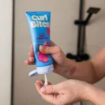 Curl Bites Multi Protein Deep Conditioner kék tubusos mélykondicionáló málnákkal rózsaszín háttér előtt.