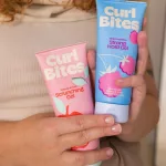 Női kézben tartott rózsaszín Curl Bites Scrunching Gel és kék Strong Hold Gel tubusos hajformázó