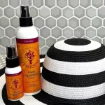 Két különböző méretű Jessicurl Awe Inspiraling Spray szórófejes flakon fekete-fehér csíkos nyári kalap mellett.